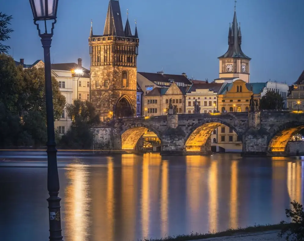 Historic Charles Bridge at dusk with illuminated towers and reflections on the Vltava River.