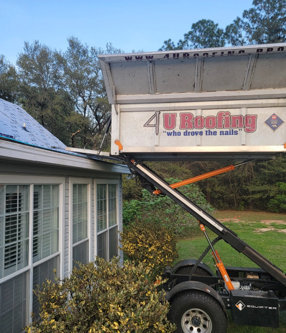 A dumpster is tipped over a roof, spilling debris.